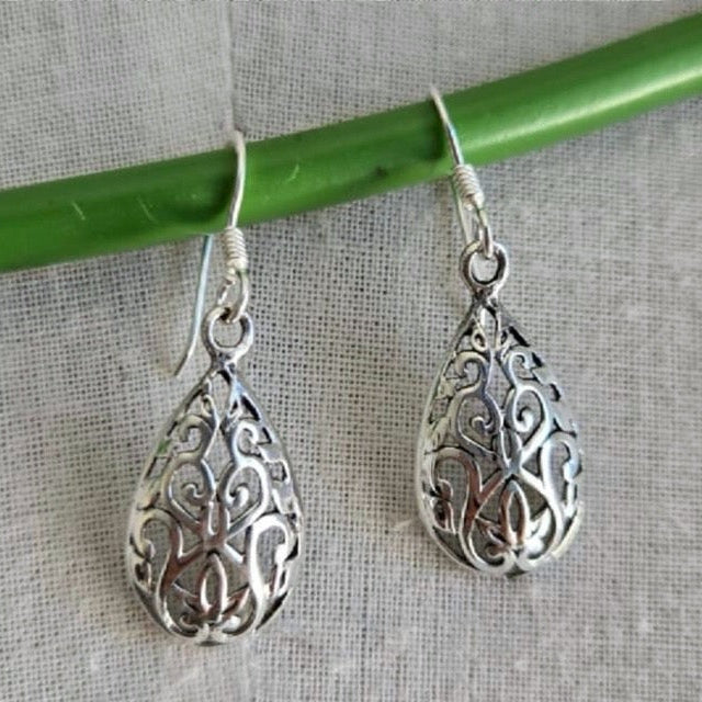 Silver filigree teardrop earrings hanging on a green rod against a gray background