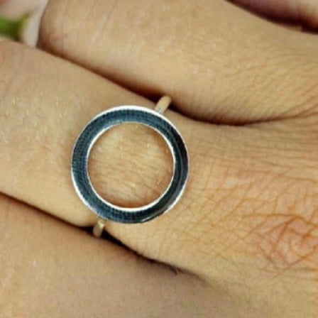 A sterling silver ring with a simple silver circle design on top, worn on a person's finger.