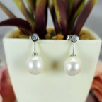 A pair of sterling silver drop earrings with freshwater pearl embellishments, displayed in a white pot with a green plant.