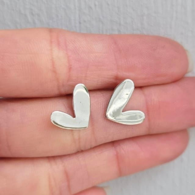 Silver heart-shaped earrings on a hand with a light background