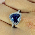 A sterling silver ring with a triangular-cut blue cubic zirconia stone and smaller clear stones around it, displayed on a person's hand.
