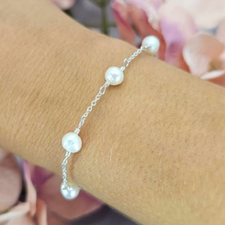A sterling silver bracelet with freshwater pearls in a link pattern, displayed on a person's wrist.