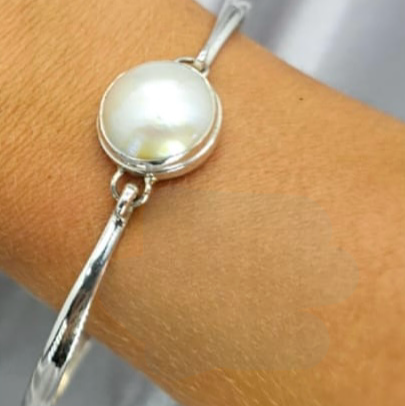 A sterling silver bangle bracelet with a white Mabe pearl on a person's wrist.