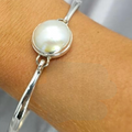 A sterling silver bangle bracelet with a white Mabe pearl on a person's wrist.