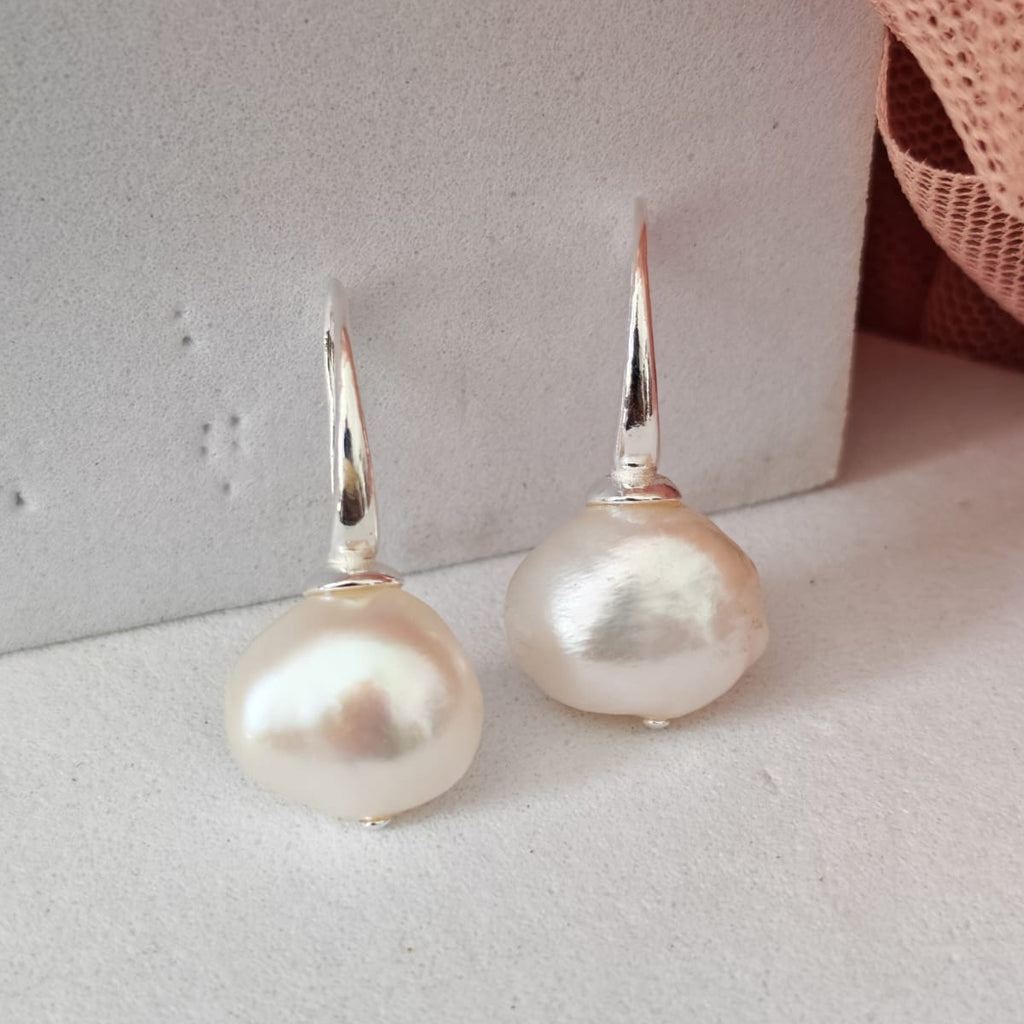 Pearl earrings on a light gray surface with a pink woven basket in the background