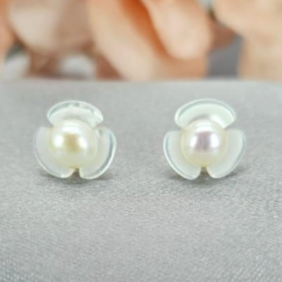 A pair of mother of pearl flower stud earrings with a sterling silver band and a central freshwater pearl.