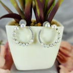 A pair of large white circle earrings with freshwater pearl accents, displayed in a white vase with green leaves.