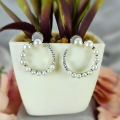 A pair of large white circle earrings with freshwater pearl accents, displayed in a white vase with green leaves.