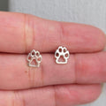 Silver paw print earrings on a hand with a light background