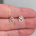 Silver paw print earrings on a hand with a light background