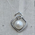 Silver pendant with a pearl on a textured fabric background