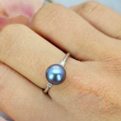 An adjustable ring with a blue freshwater pearl and cubic zirconia detail, displayed on a person's hand.