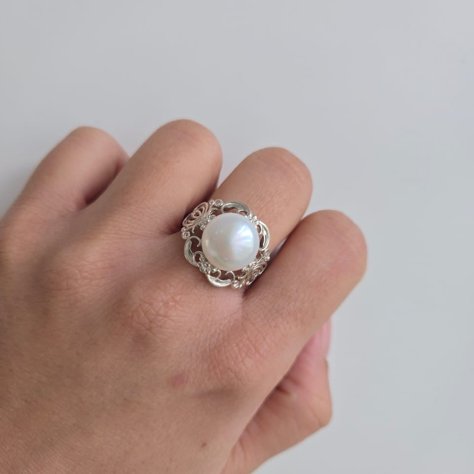 Hand wearing a ring with a pearl on a plain background