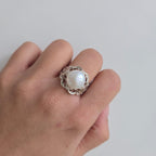 Hand wearing a ring with a pearl on a plain background