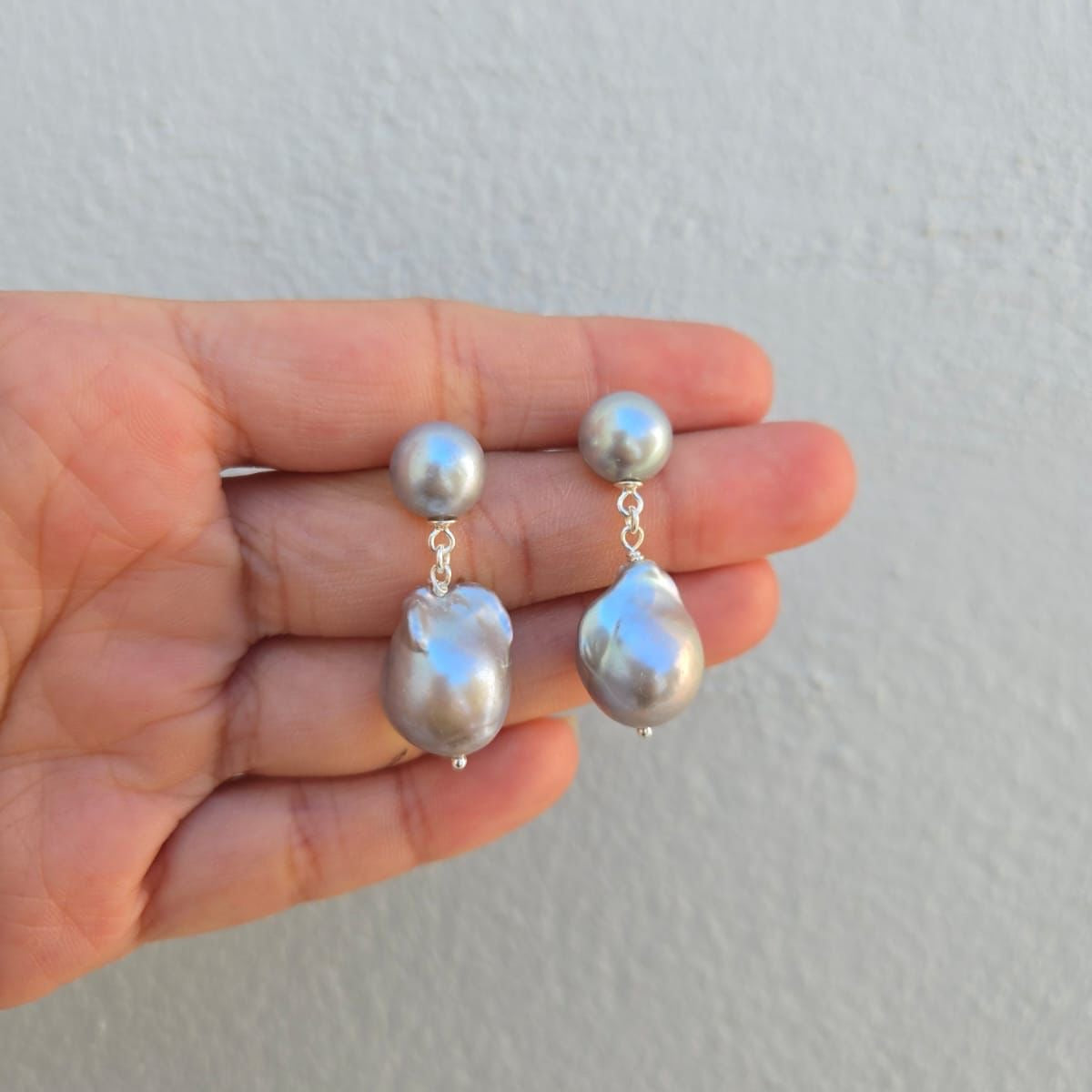 Pearl earrings held in a hand against a plain background