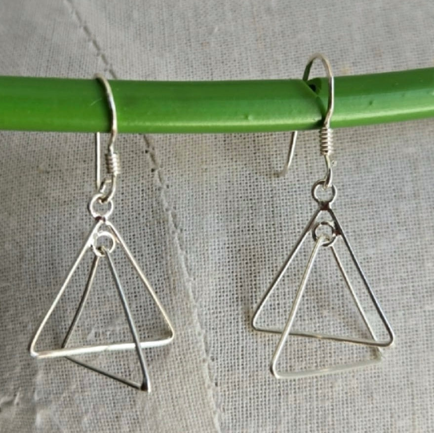 Silver triangle earrings hanging from a green rod on a textured surface.