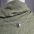 Silver necklace with a round pendant on a green fabric surface