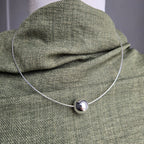 Silver necklace with a round pendant on a green fabric surface