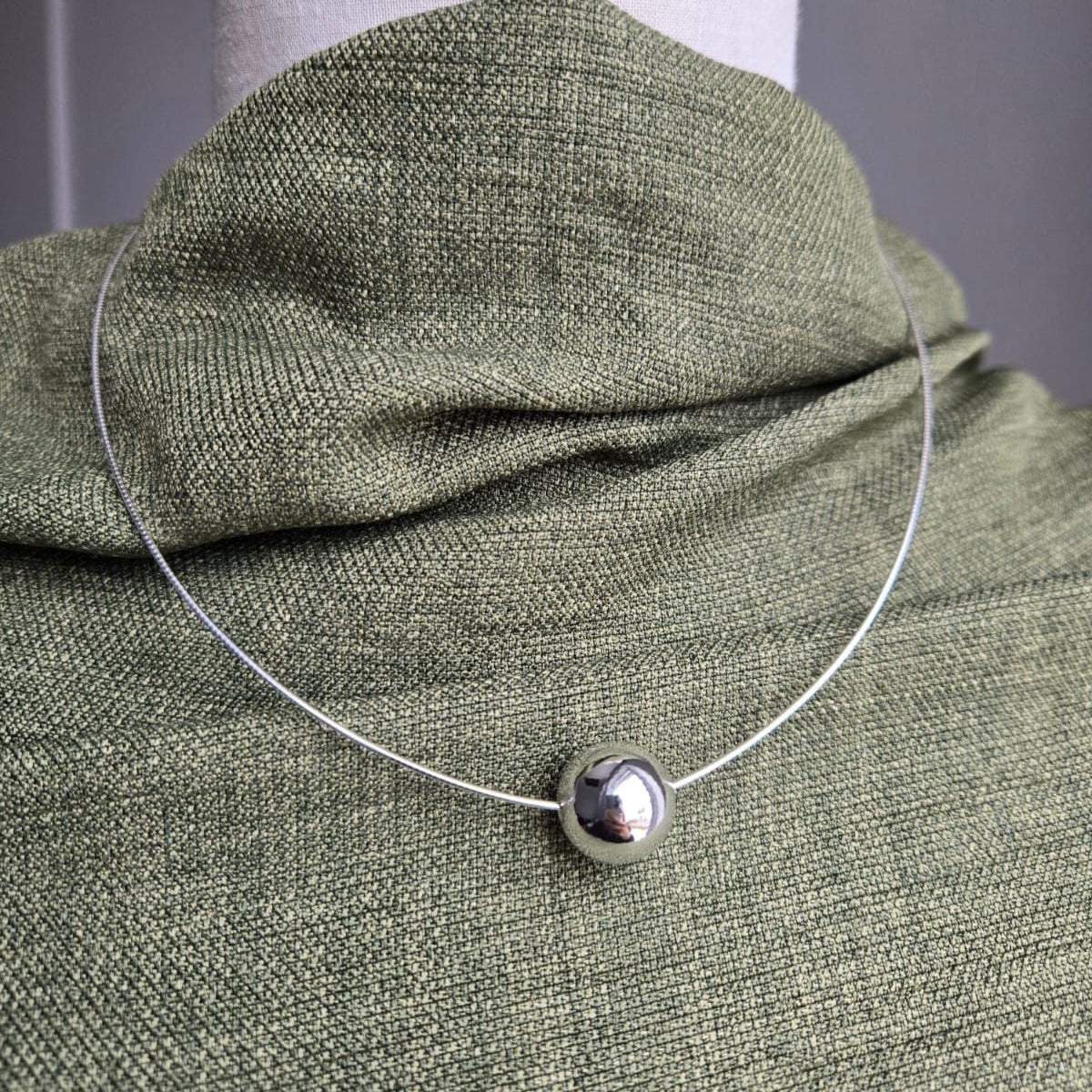 Silver necklace with a round pendant on a green fabric surface