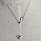 Necklace with a bee and daisy pendant on a gray background