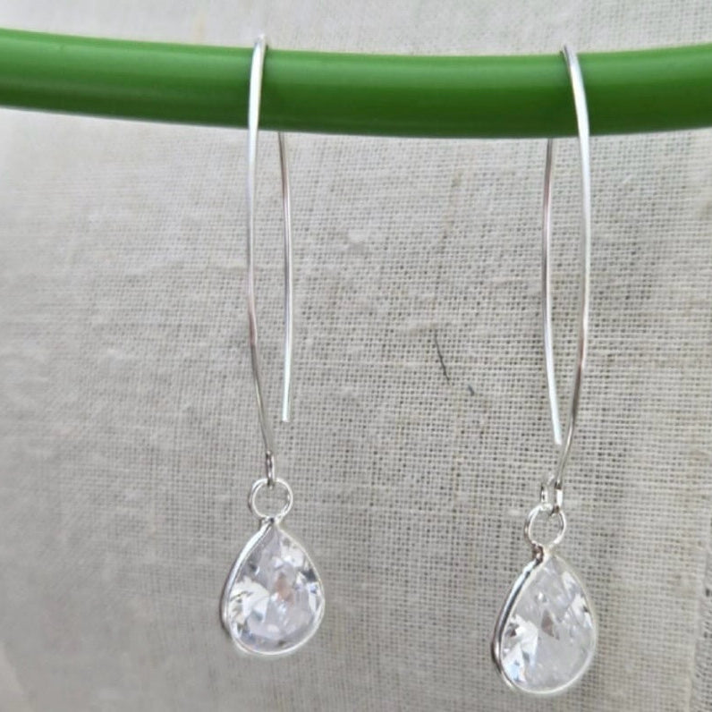 Silver teardrop earrings hanging on a green rod against a gray background