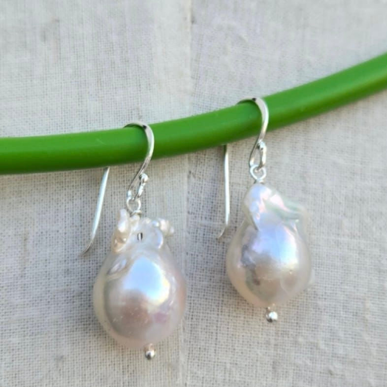 Pearl earrings hanging on a green stick against a beige background