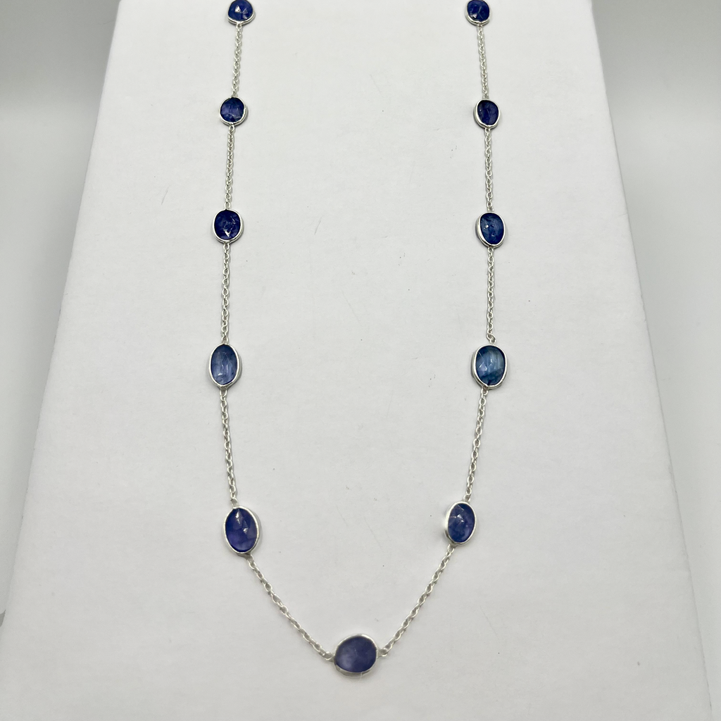A necklace with oval-shaped tanzanite stones set in a chain design, displayed on a white mount.