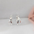 Silver hoop earrings on a light gray surface with a pink mesh bag in the background.