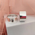 Two silver rings on a white surface with a pink fabric background