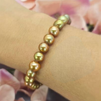 A gold-colored freshwater pearl bracelet worn on a person's wrist, with a background of pink flowers.