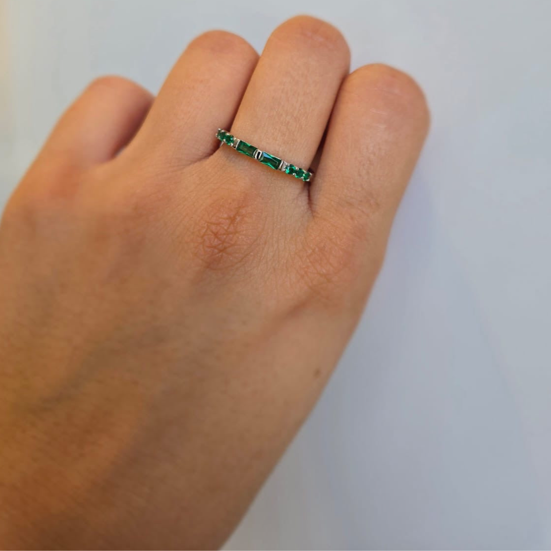 A green stacking ring with cubic zirconia stones on a person's hand against a white background.