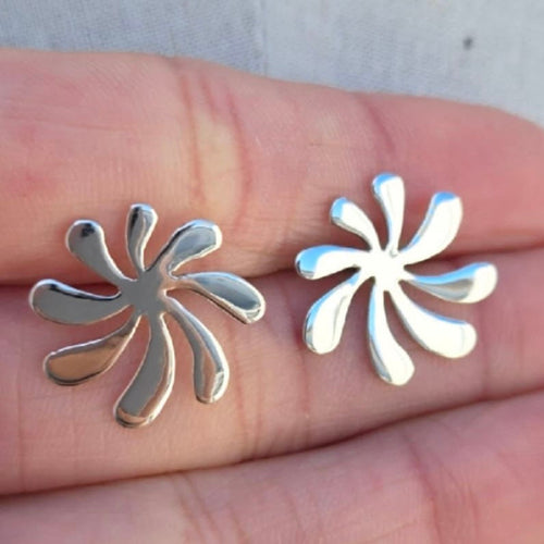 Silver floral earrings held between fingers against a neutral background
