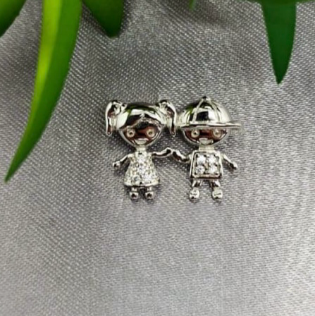 A sterling silver pendant featuring a boy and girl design, placed on a textured surface with a green plant in the background.