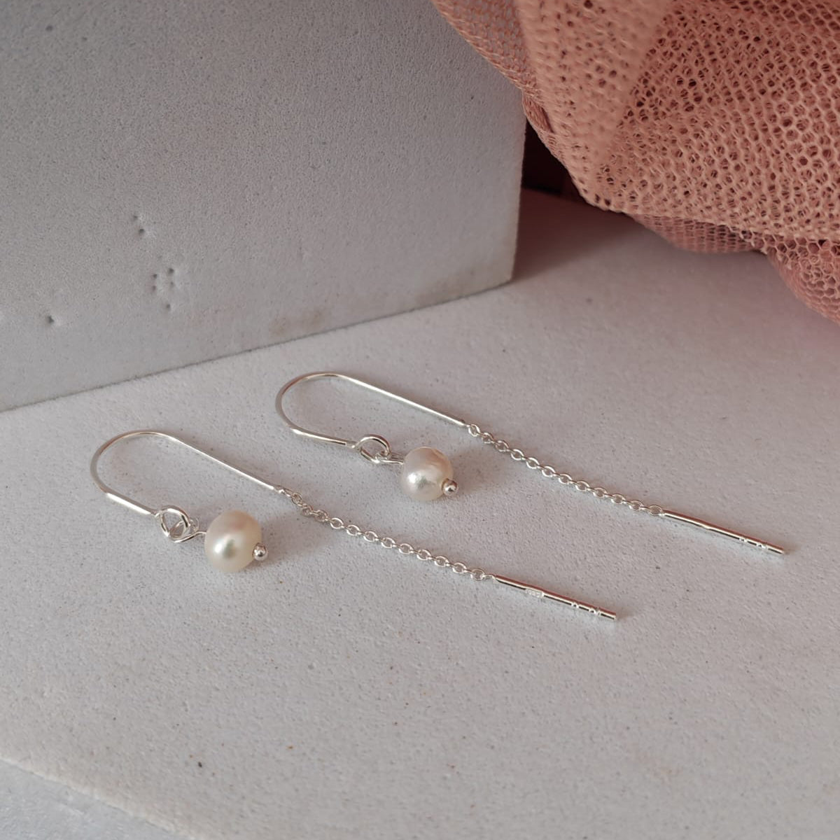Silver earrings with pearls on a light surface