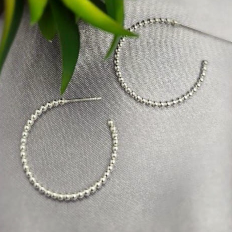 A pair of sterling silver rope hoop earrings with small beads, displayed on a linen surface.