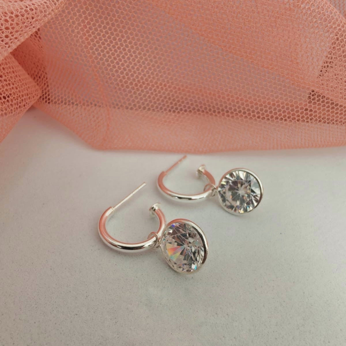 Silver hoop earrings with clear gemstones on a light pink fabric background