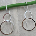 Pair of silver hoop earrings hanging on a green rod against a textured beige background