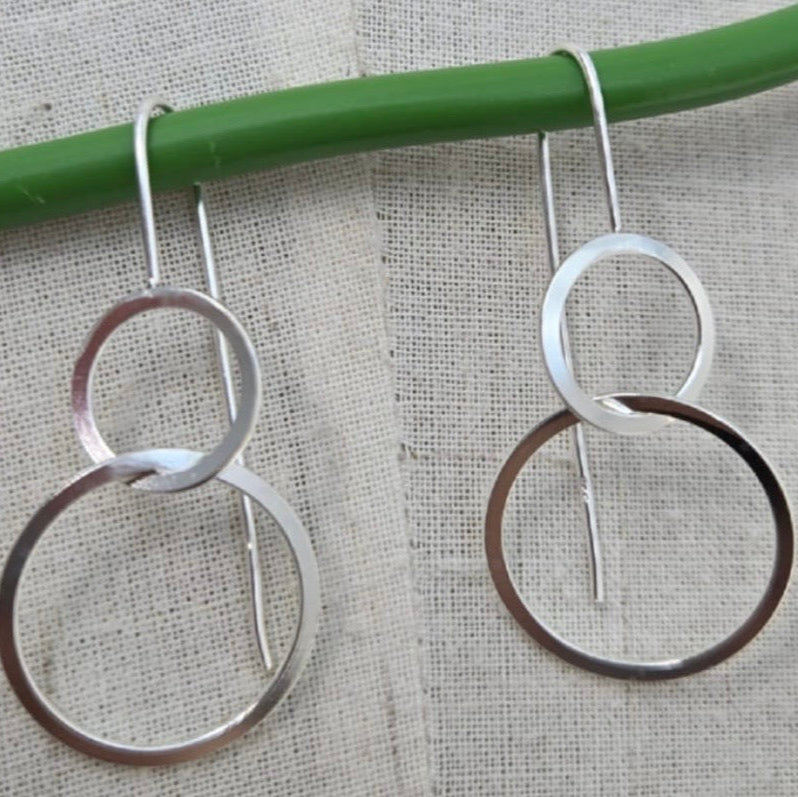 Pair of silver hoop earrings hanging on a green rod against a textured beige background