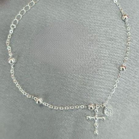 A sterling silver bracelet with small round bobbles and a dangling cross, displayed against a grey background.