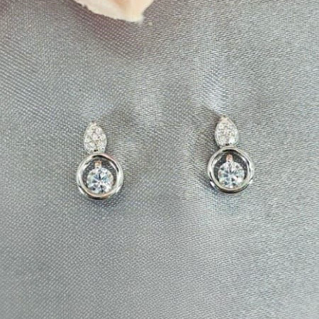Silver earrings with clear stones on a gray surface with a pink flower in the background