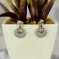 A pair of sterling silver pavé studs earrings with cubic zirconia, displayed in a white pot with purple and green plants in the background.