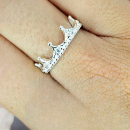 A woman's hand displaying a silver crown-shaped ring with cubic zirconia detailing on her finger.