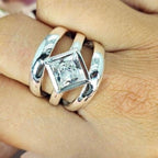 A three-band sterling silver ring with diamond-shaped cubic zirconia centerpiece, displayed on a person's hand.