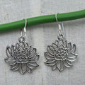 Silver lotus flower earrings on a gray background with a green stick.