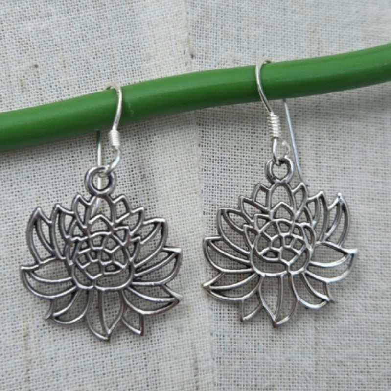 Silver lotus flower earrings on a gray background with a green stick.