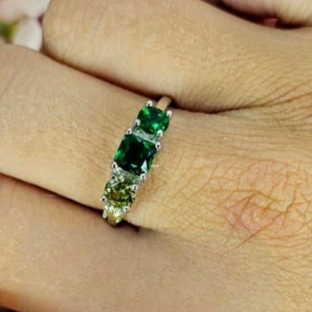 A sterling silver ring with three shades of green cubic zirconia stones set on a hand.
