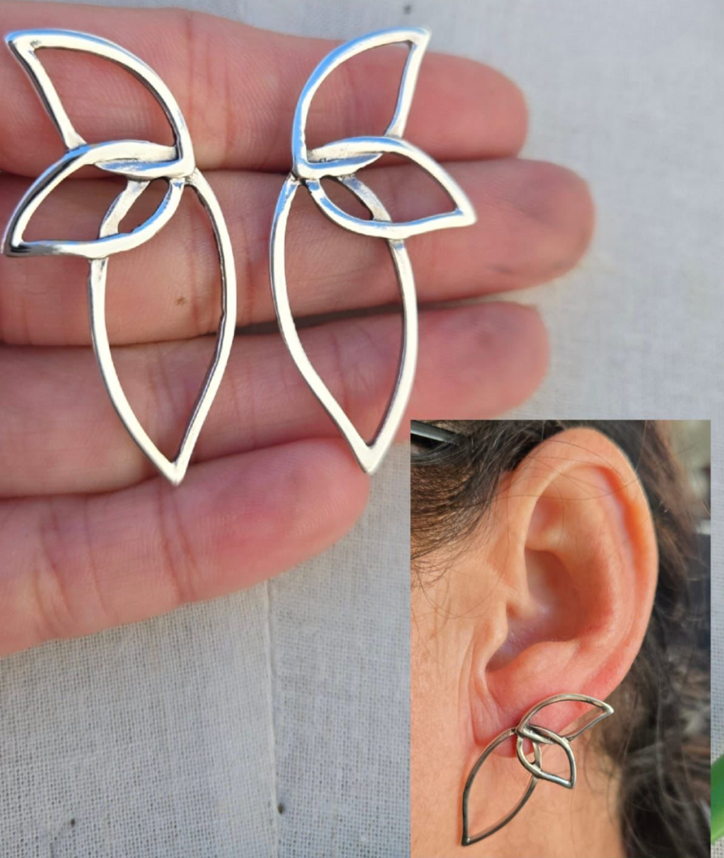 Silver leaf-shaped earrings held between fingers with a close-up of an ear wearing one of the earrings.