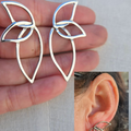 Silver leaf-shaped earrings held between fingers with a close-up of an ear wearing one of the earrings.