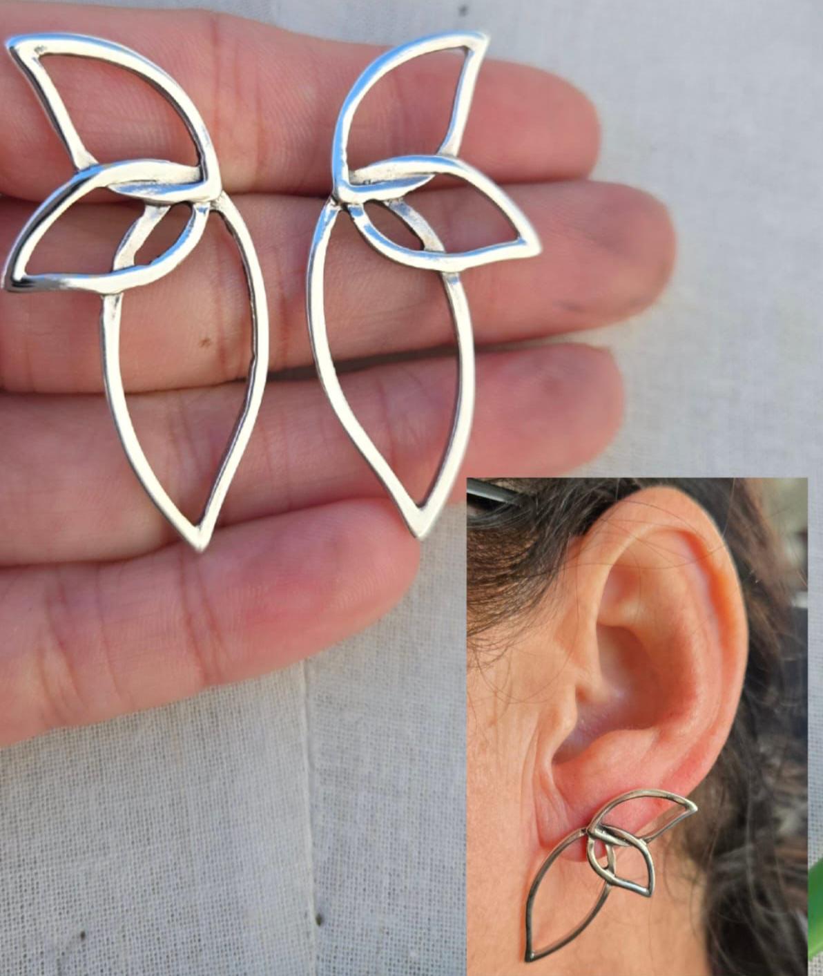 Silver leaf-shaped earrings held between fingers with a close-up of an ear wearing one of the earrings.