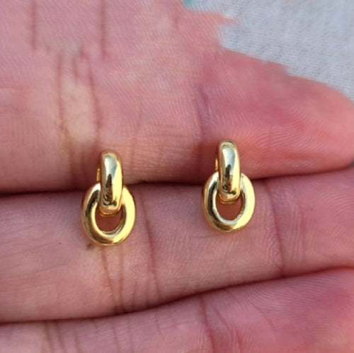Gold hoop earrings held between fingers on a neutral background